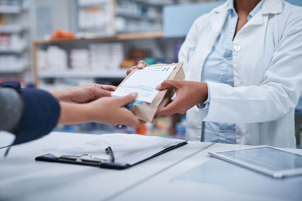 Female pharmacist handing prescription bag over to customer
